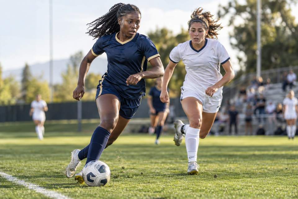 Women's soccer player pushing the ball past a defender